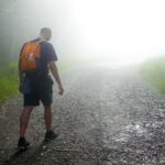 a man with a backpack walking down a foggy road